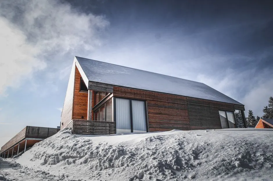 A contemporary wooden cabin with a snow-covered roof in a serene winter setting.